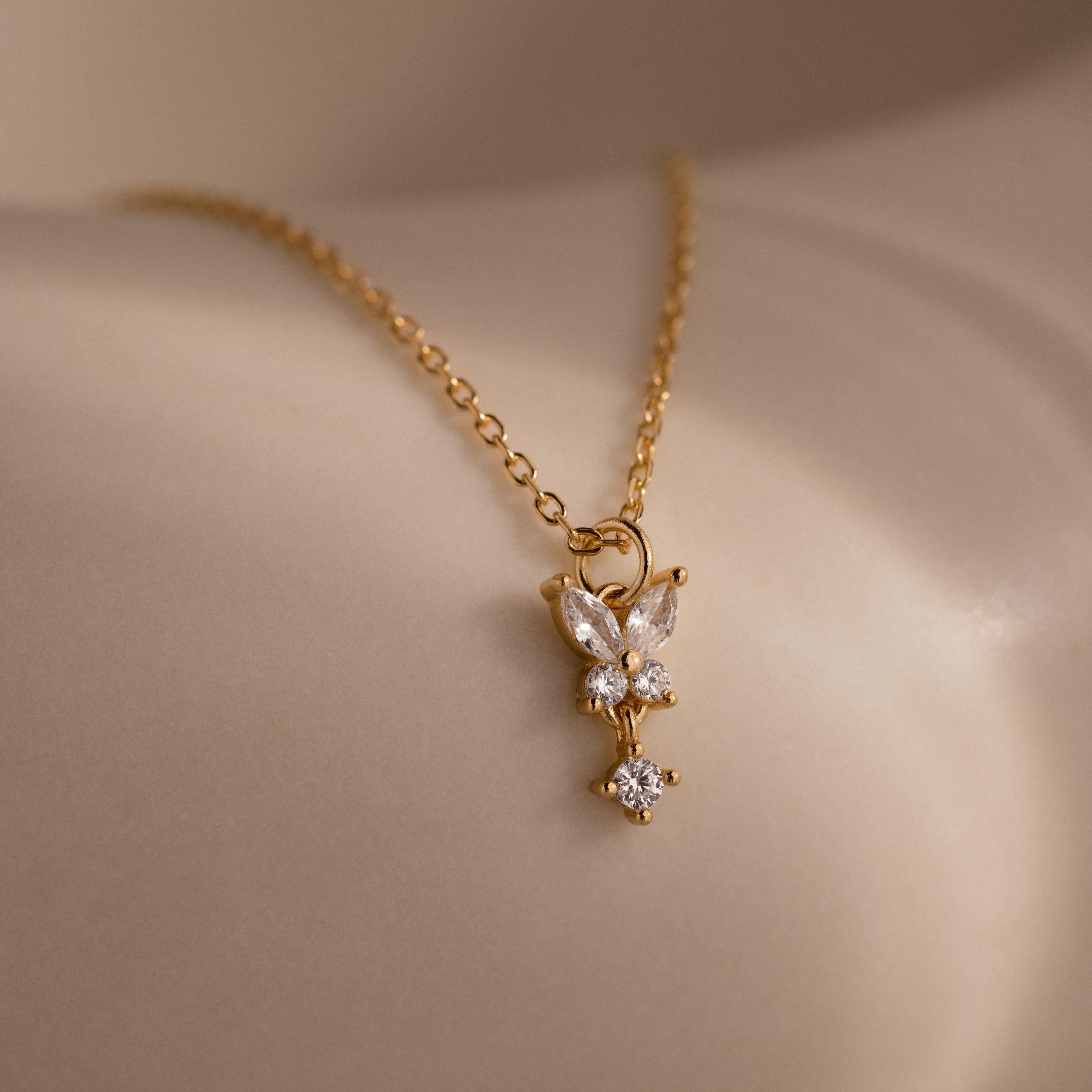 The Butterfly Drop Necklace in 18K Gold features a delicate butterfly pendant adorned with sparkling clear crystals—a stunning piece of nature-inspired jewelry that rests beautifully on the skin.