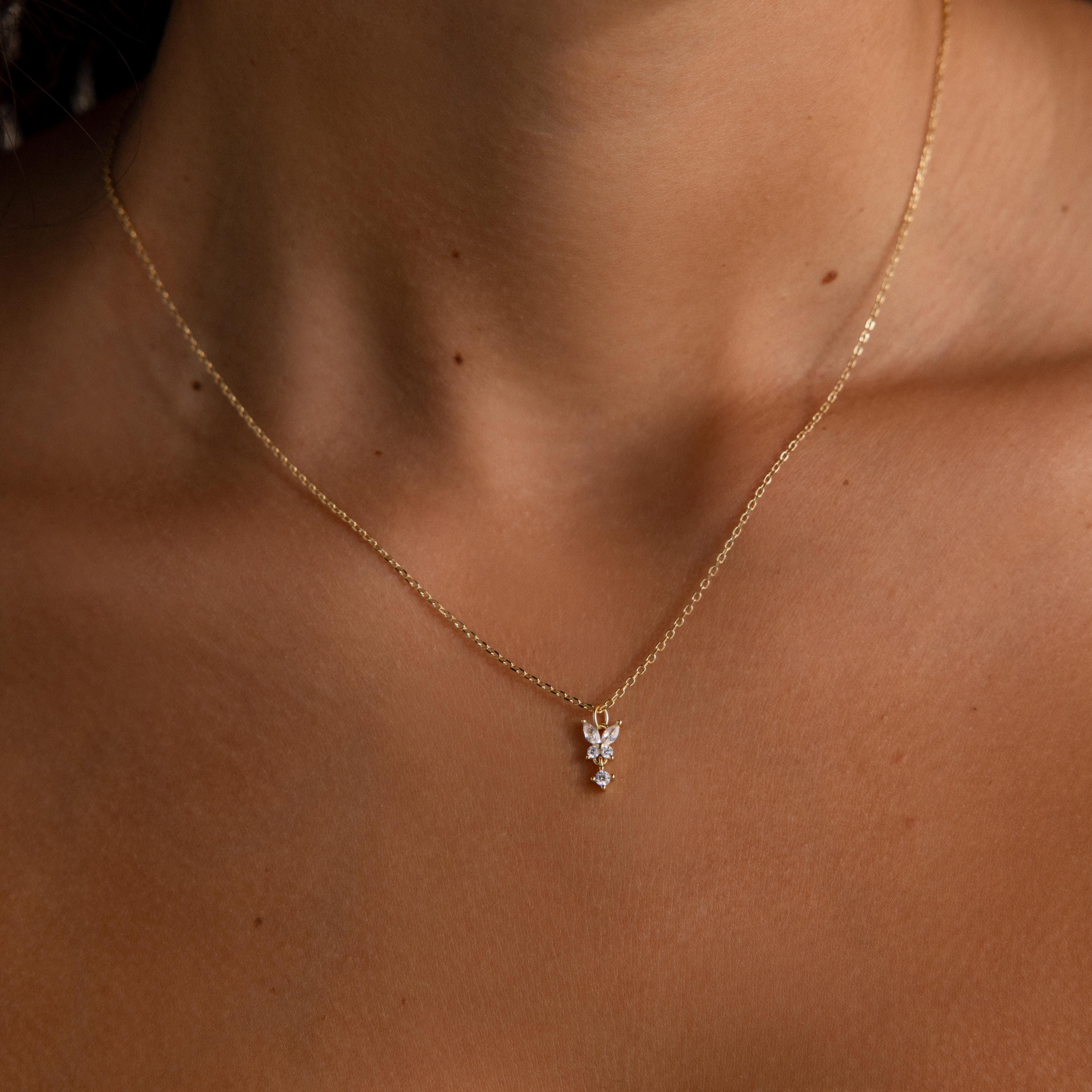 Butterfly Drop Necklace, a delicate gold piece with a small butterfly pendant, rests gracefully on a womans neck and collarbone.