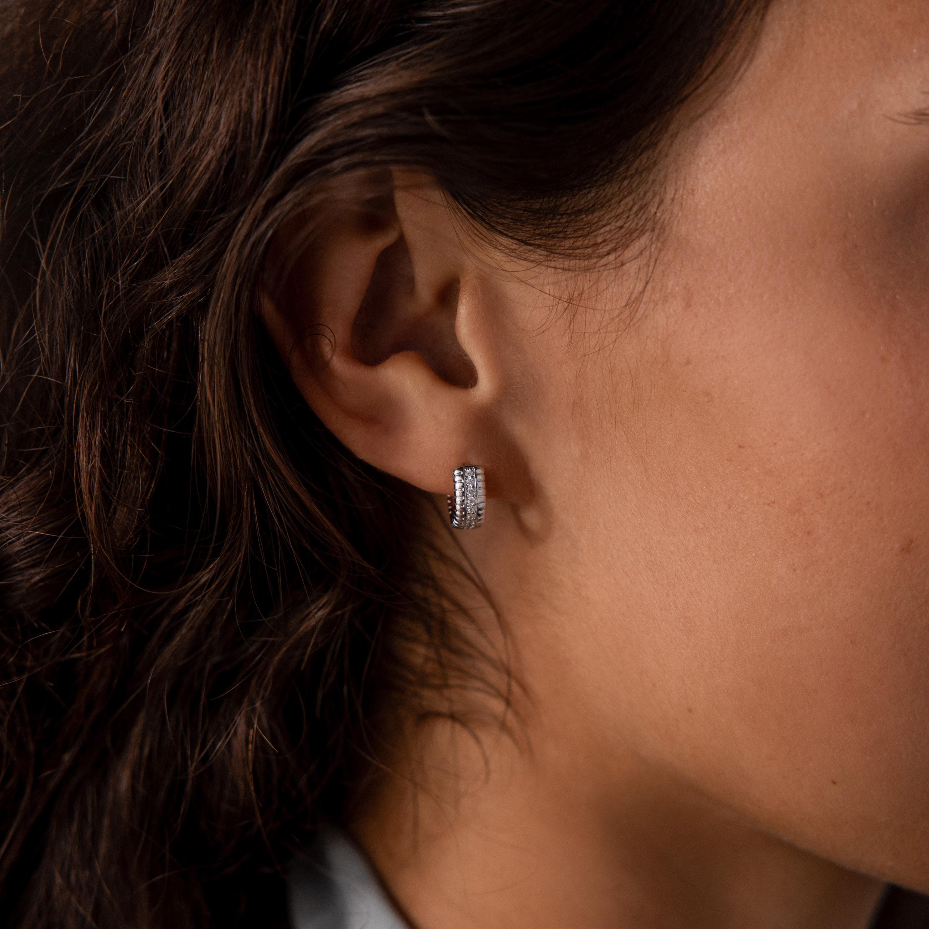 Close-up of a womans ear wearing Ribbed Pave Huggies in Sterling Silver—small hoops with multiple rows of sparkling cubic zirconia stones.