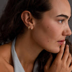 A woman with wavy hair and a halter top gazes thoughtfully to the side, wearing two pairs of Ribbed Pave Huggies.