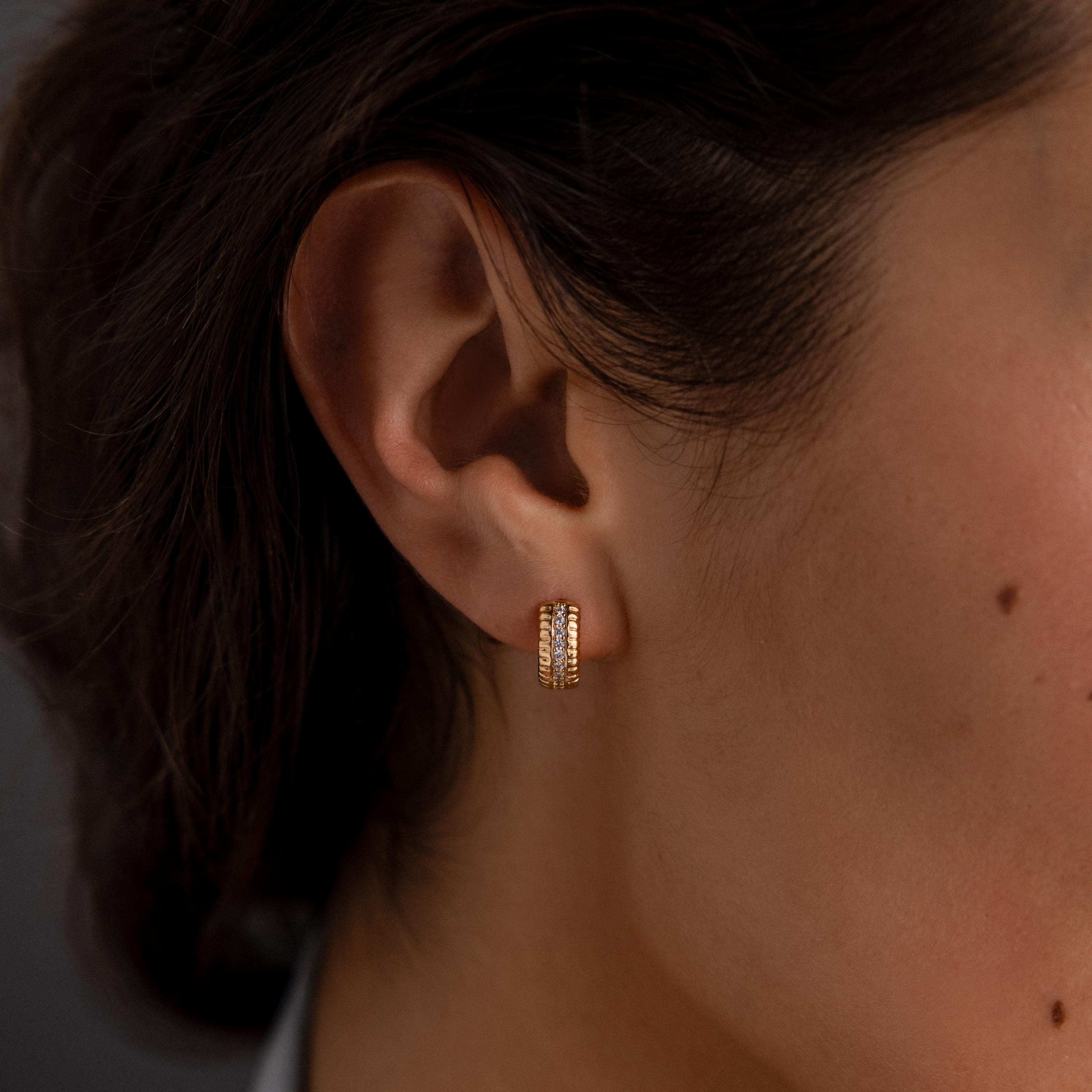 Close-up of a womans ear wearing Ribbed Pave Huggies in 18K Gold, chunky hoop earrings embellished with sparkling cubic zirconia stones.