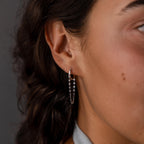 Close-up of a womans ear adorned with the Mirror Chain Huggies in Sterling Silver, paired with a delicate chain, against her curly brown hair.