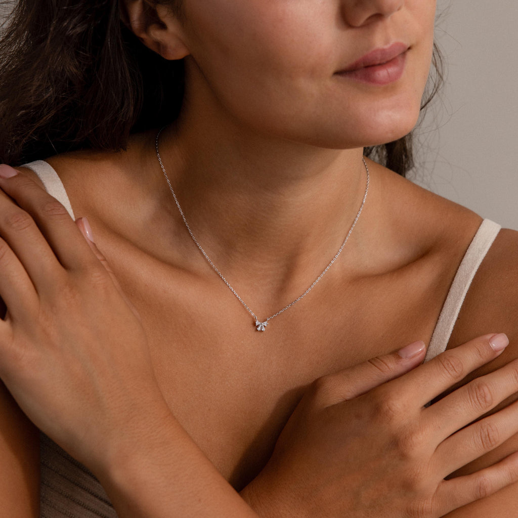 Woman wearing a Diamond Bow Necklace in Sterling Silver, featuring a small bow pendant, hands gently touching her shoulders.