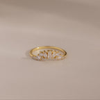 The Diamond Curve Cluster Ring features an baguette stone and a row of clear marquise and round diamonds set in gold, displayed on a smooth, neutral surface.