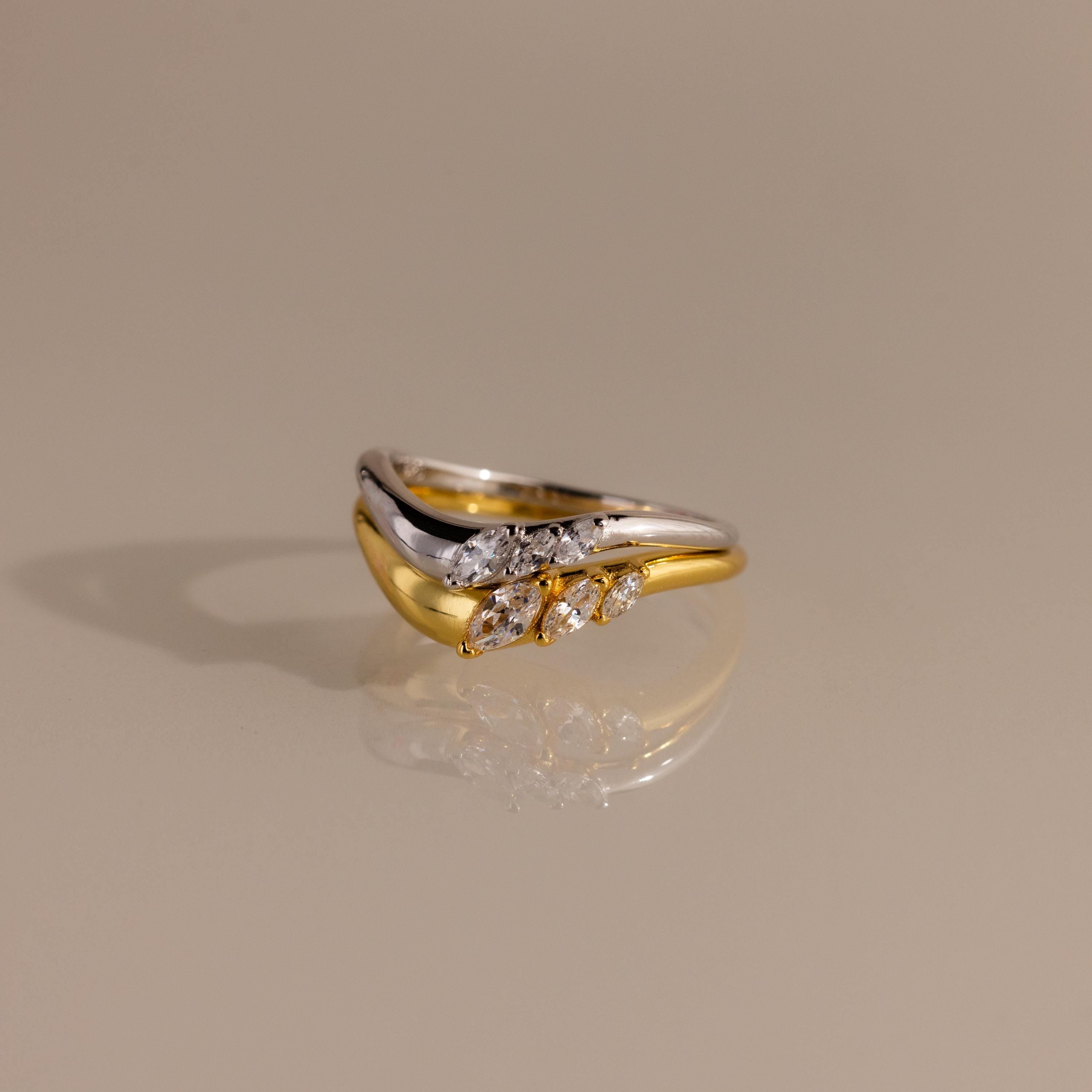 Gold and silver stacked curve rings featuring marquise cut stones, designed in a modern wavy silhouette with a reflective finish.