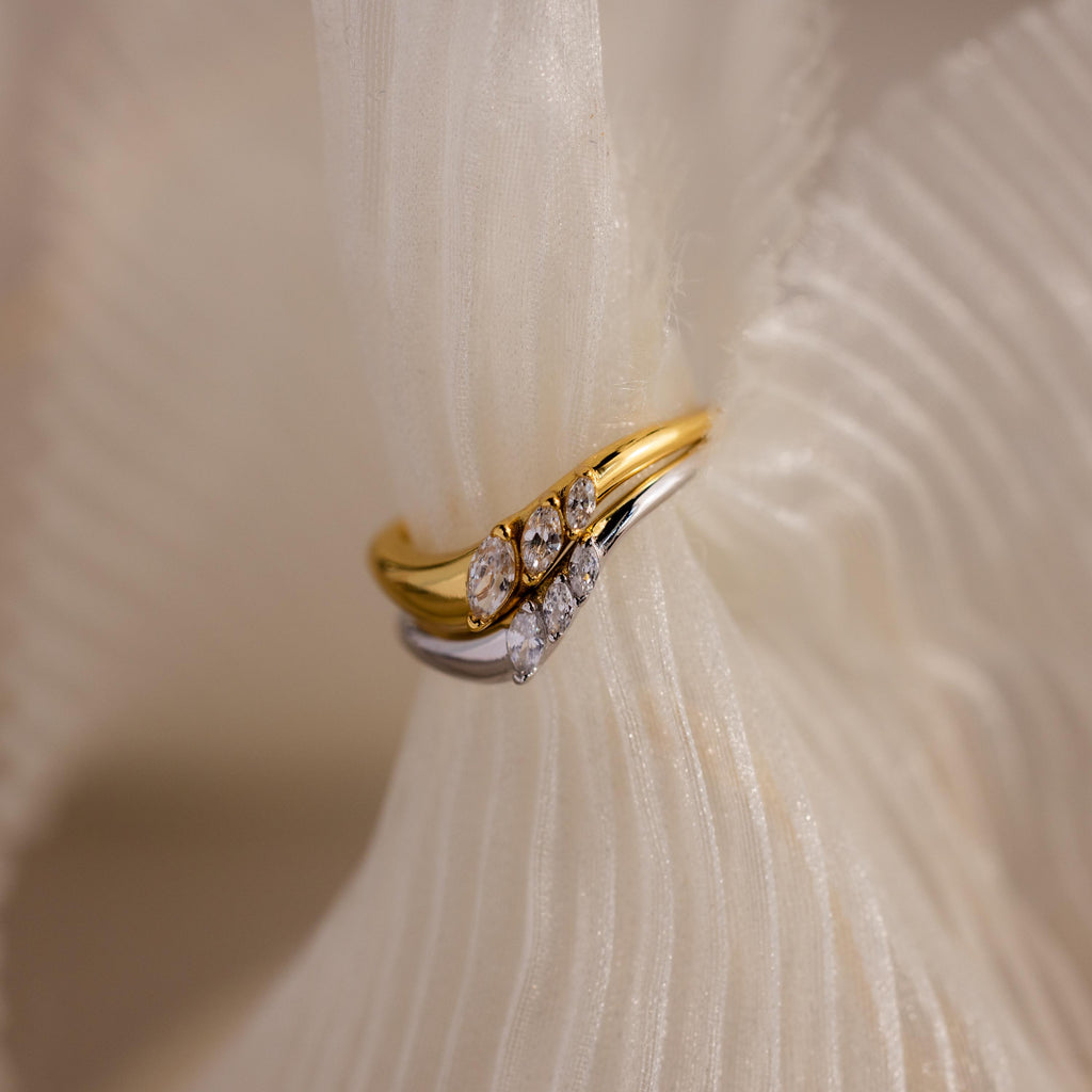 Gold and silver curve rings with marquise cut stones stacked together, styled on soft textured fabric for an elegant display.