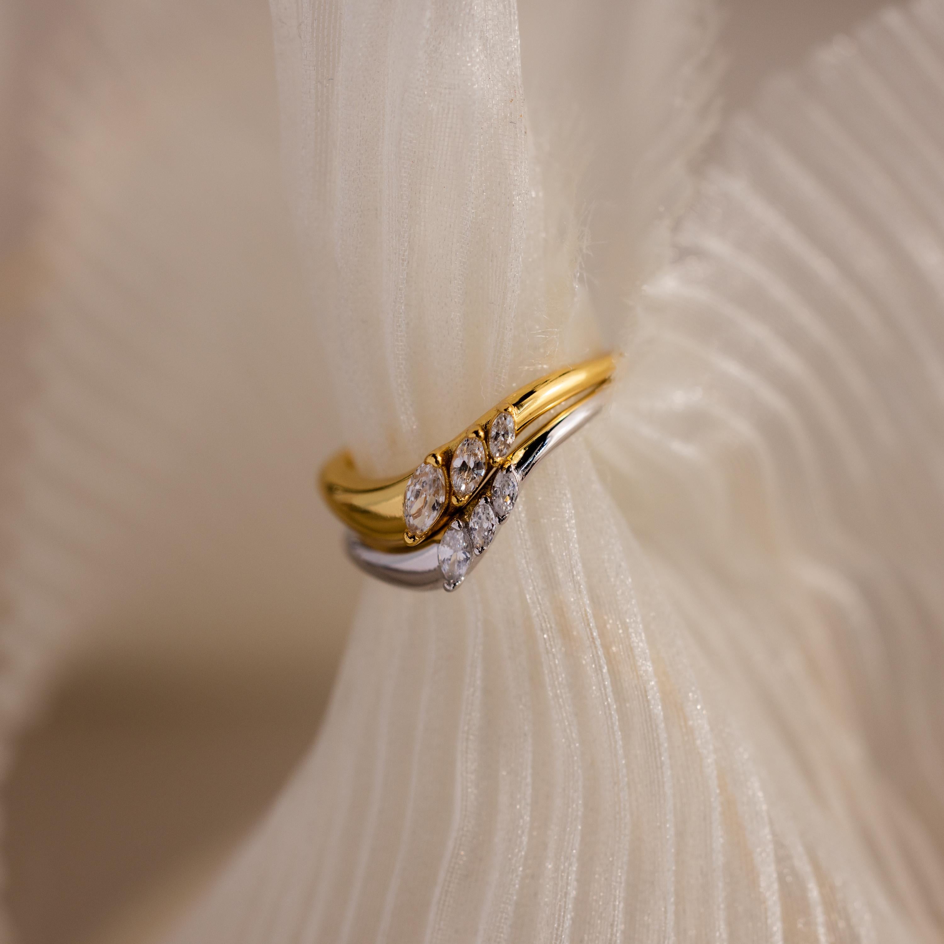 Gold and silver curve rings with marquise cut stones stacked together, styled on soft textured fabric for an elegant display.