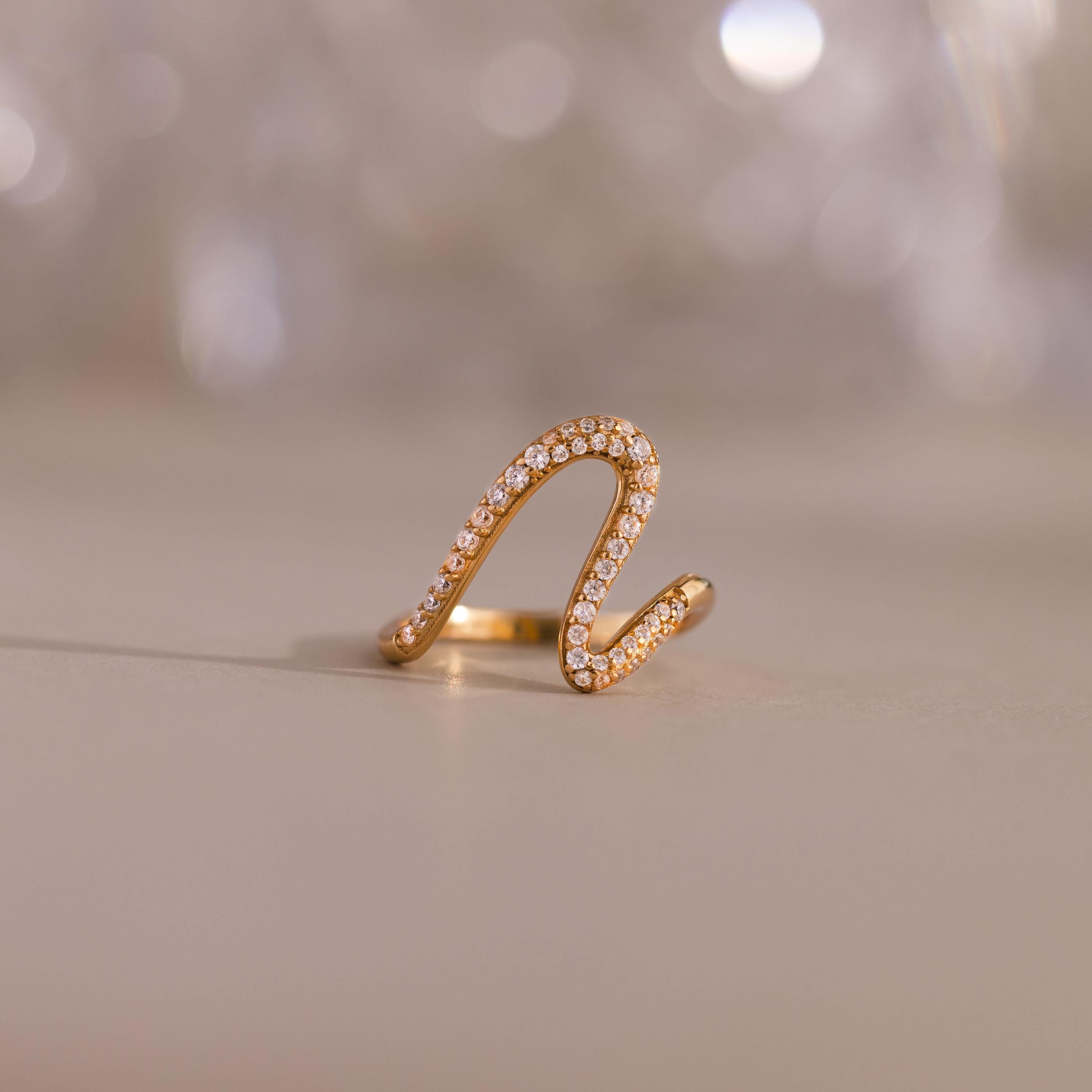 The Pave Wave Ring, crafted in gold and accented with pavé-set diamonds, is elegantly displayed against a smooth surface and blurred background. Ideal as a stacking ring for adding subtle sophistication to any look.