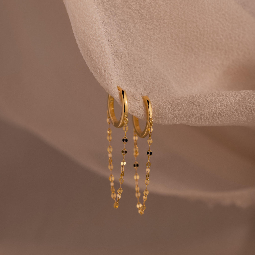 The Mirror Chain Huggies are gold hoop earrings featuring delicate chain details, perfect for adding minimalist elegance to any look.