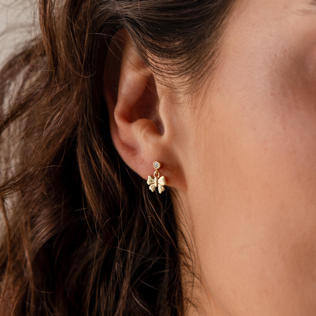 Close-up of a womans ear wearing gold flower-shaped earrings with gemstone studs, perfect for lovers of delicate jewelry or for pairing with the Bow Drop Studs for an elegant, coordinated look.