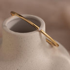 A Skinny Diamond Bangle in 18K Gold with a delicate diamond detail rests gracefully on a smooth, speckled ceramic vase.