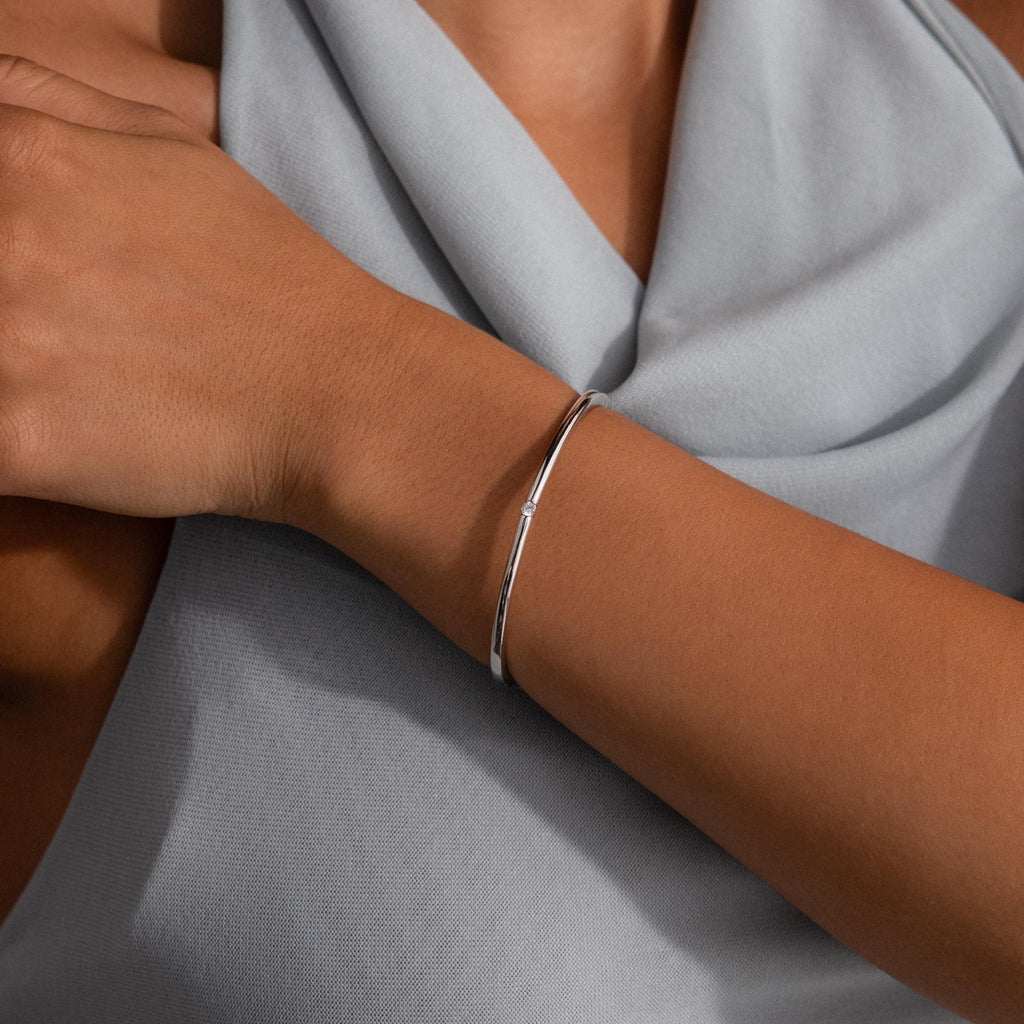 A minimalist look features the Skinny Diamond Bangle in White Gold on the wrist, stylishly paired with a light gray draped top.