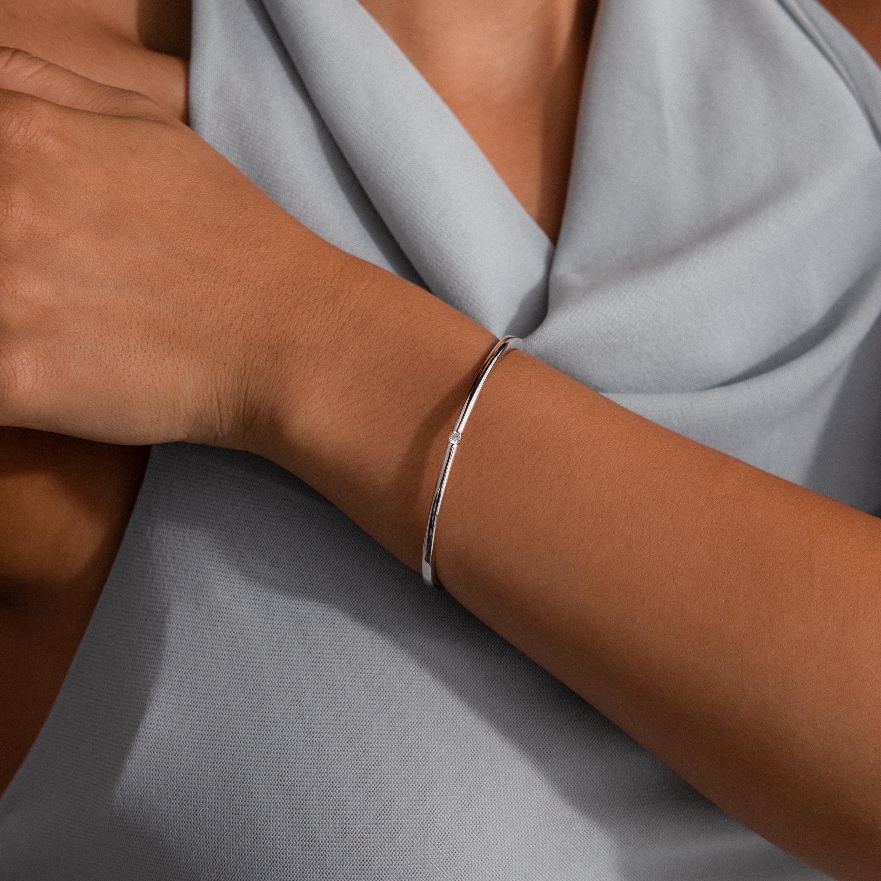 A minimalist look features the Skinny Diamond Bangle in White Gold on the wrist, stylishly paired with a light gray draped top.