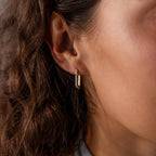 Close-up of a womans ear wearing the Dainty Pave Link Earrings in 18K Gold, featuring minimalist hoops with a row of sparkling cubic zirconia stones.