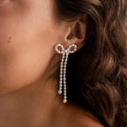 Close-up of a woman's ear wearing Pearl Bow Earrings, featuring an elegant bow design with pearl details and delicate dangling strands for a statement look.