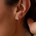 Close-up of a woman's ear wearing Birthstone Heart Hoops—small, heart-shaped earrings accented with two tiny stones—ideal for fans of delicate birthstone jewelry.