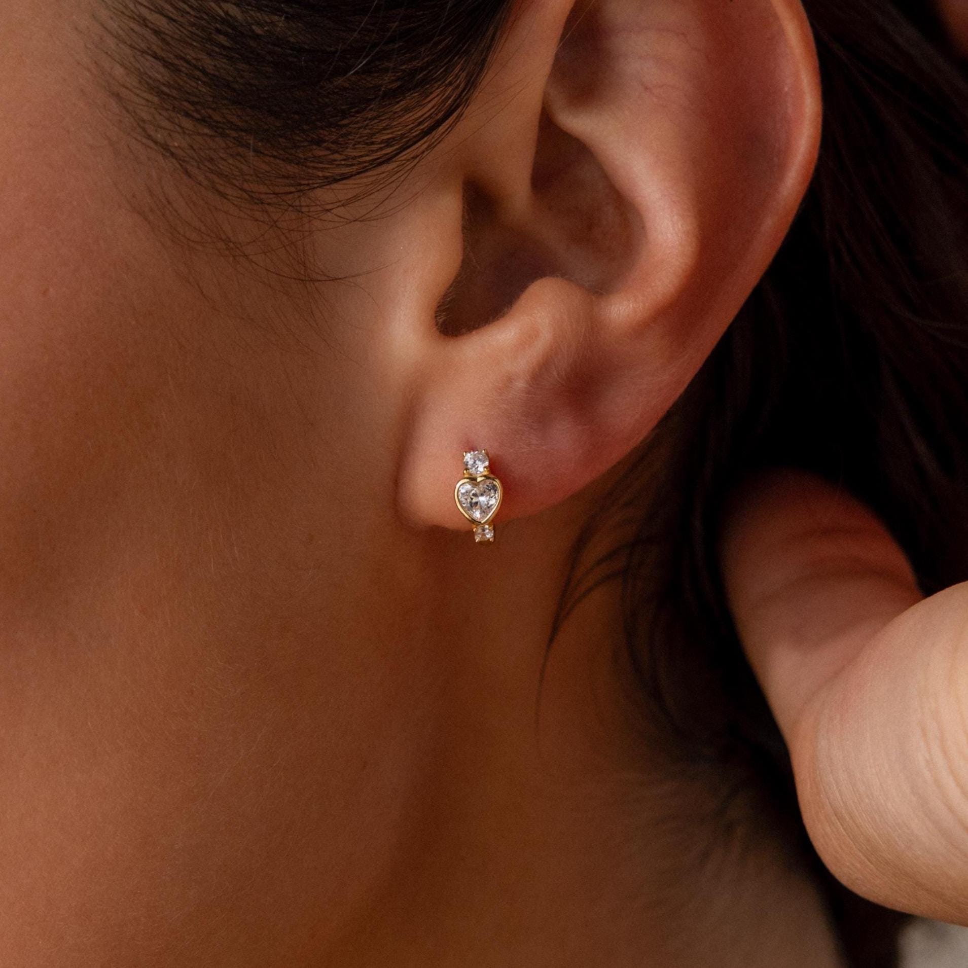 Close-up of a woman's ear wearing Birthstone Heart Hoops—small, heart-shaped earrings accented with two tiny stones—ideal for fans of delicate birthstone jewelry.