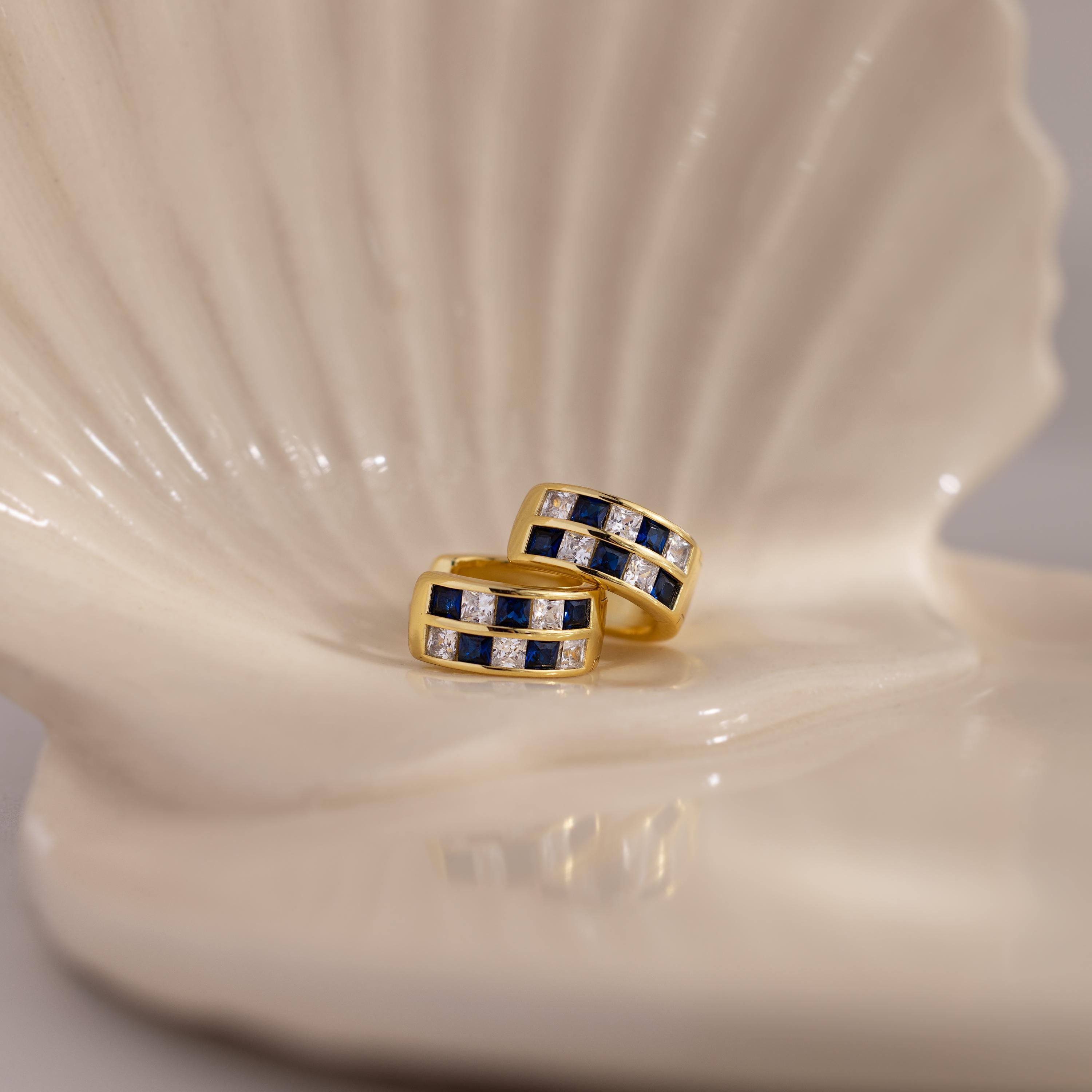 Royal Blue Checkered Huggies in 18K Gold sparkle on a glossy ceramic shell-shaped dish.