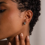 Close-up of a person’s ear wearing Royal Blue Checkered Huggies; manicured hand posed near their face.