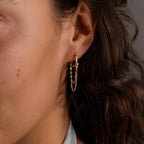 Close-up of a woman's ear wearing Duo Mirror Chain Huggies—modern gold hoops featuring dangling chains and small beads.