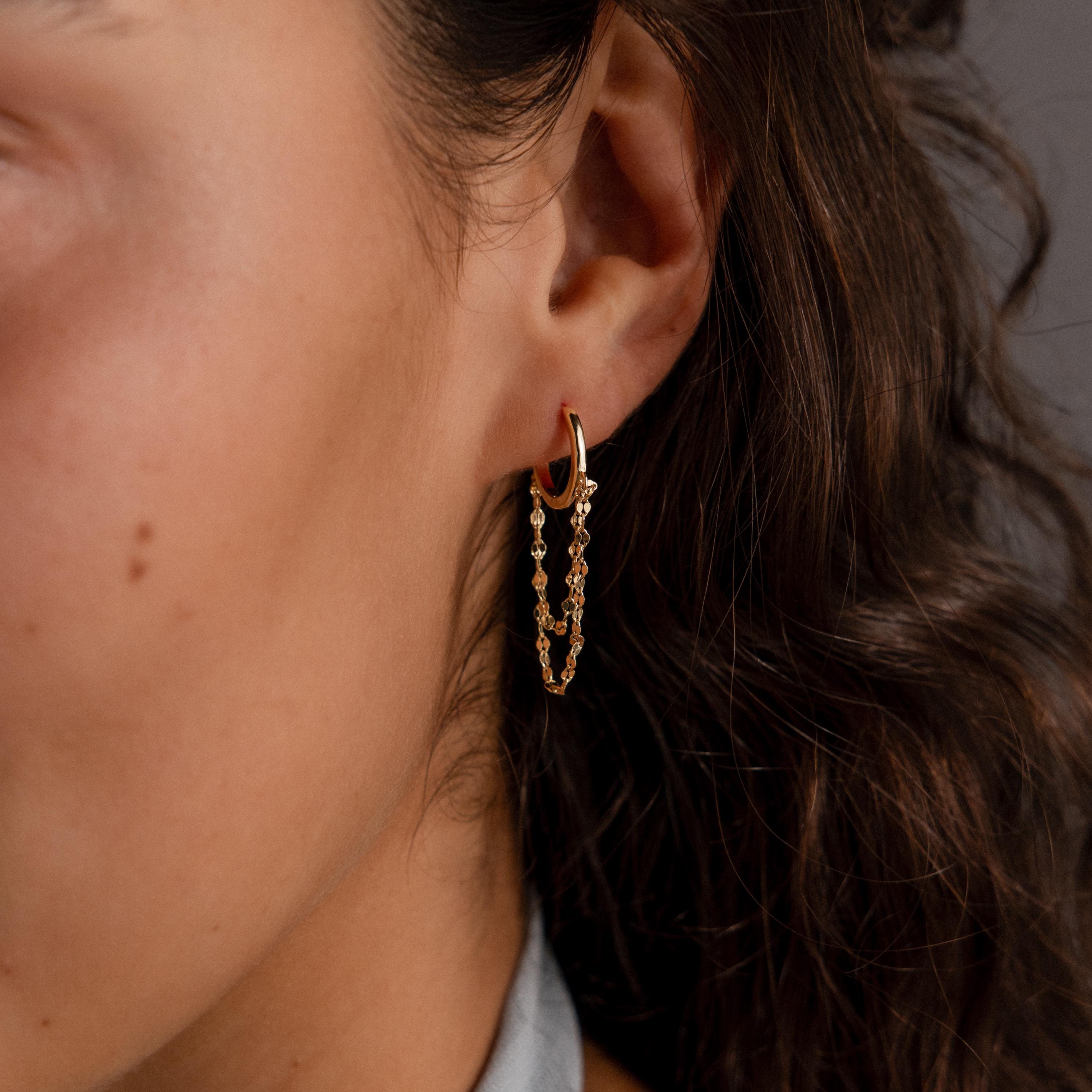 Close-up of a woman's ear wearing Duo Mirror Chain Huggies—modern gold hoops featuring dangling chains and small beads.