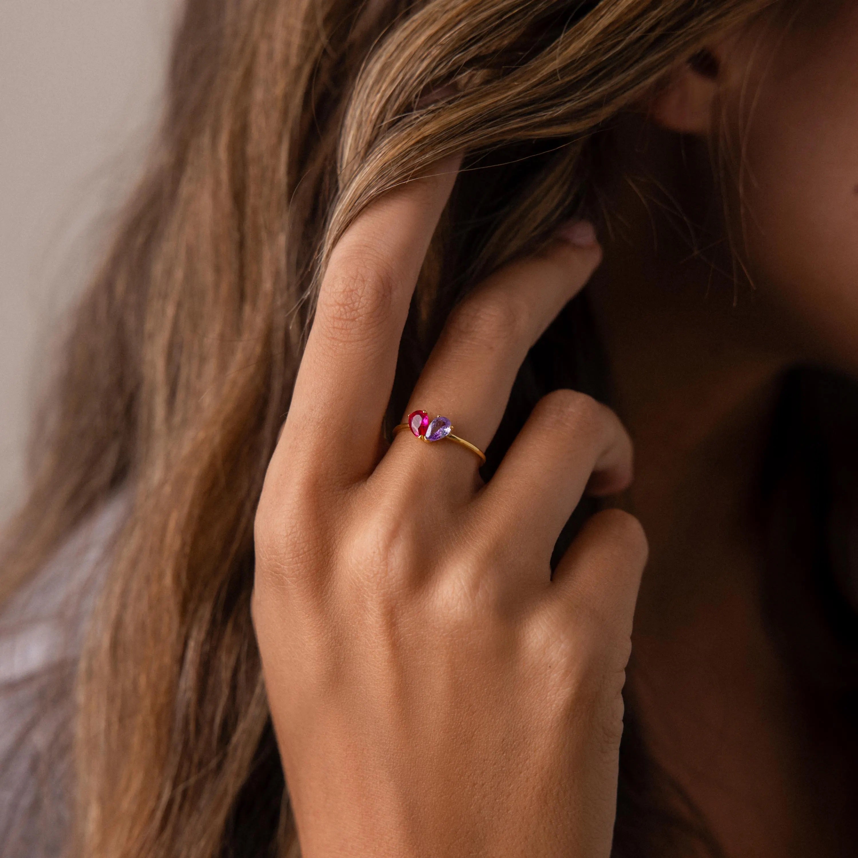Hand with long brown hair wearing the Toi et Moi Teardrop Heart Ring in 18K Gold, featuring two heart-shaped pink and purple stones.