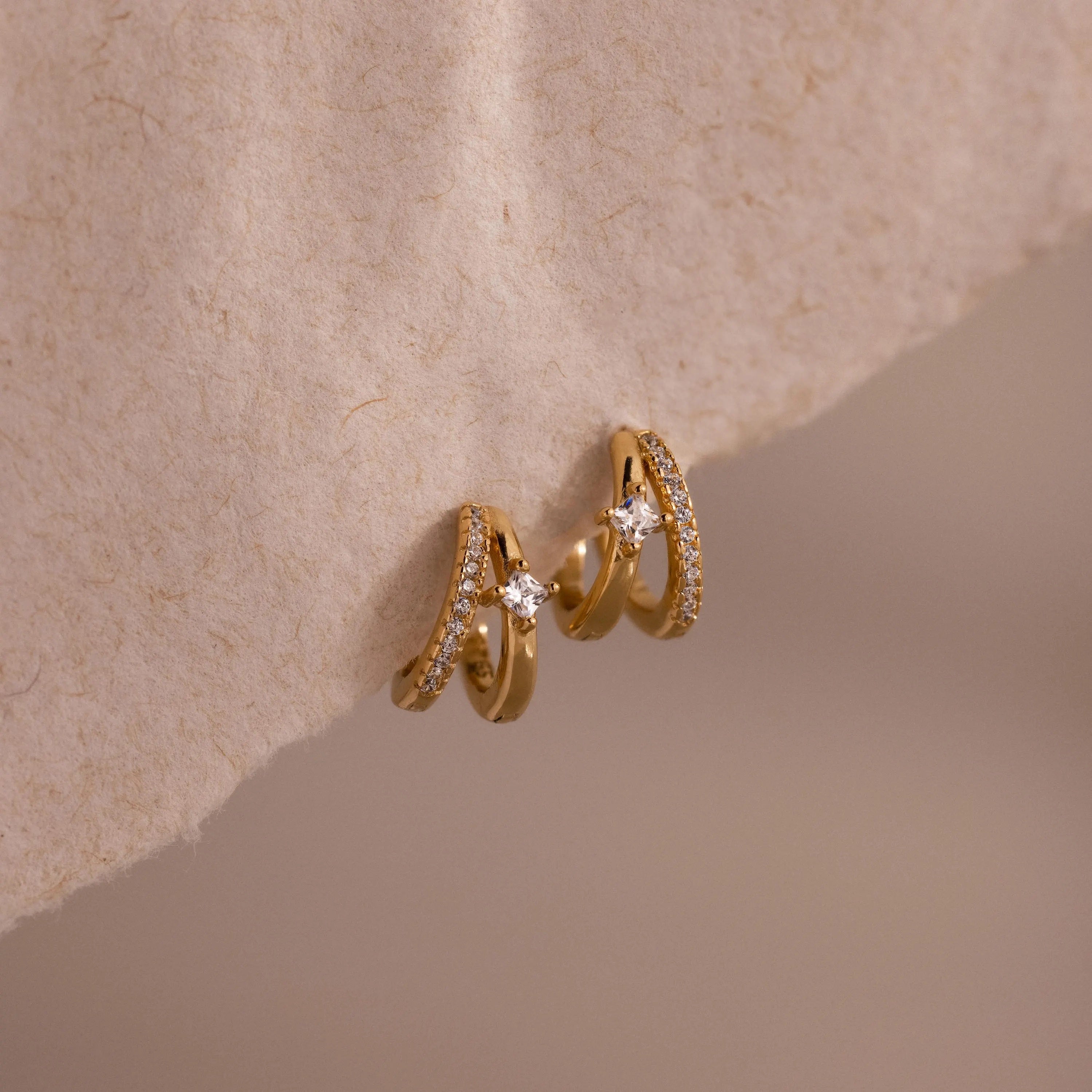 The Pave Diamond Duo Huggies sparkle on a textured beige surface, bringing timeless elegance to classic gold hoop earrings.