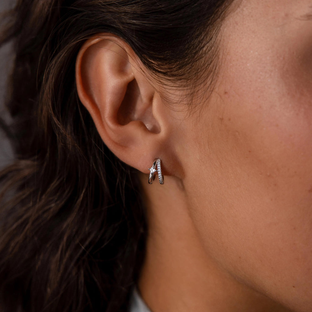 Close-up of a woman's ear wearing the Pave Diamond Duo Huggies in Sterling Silver, featuring small hoop earrings with leaf-shaped charms accented by pavé-set stones.