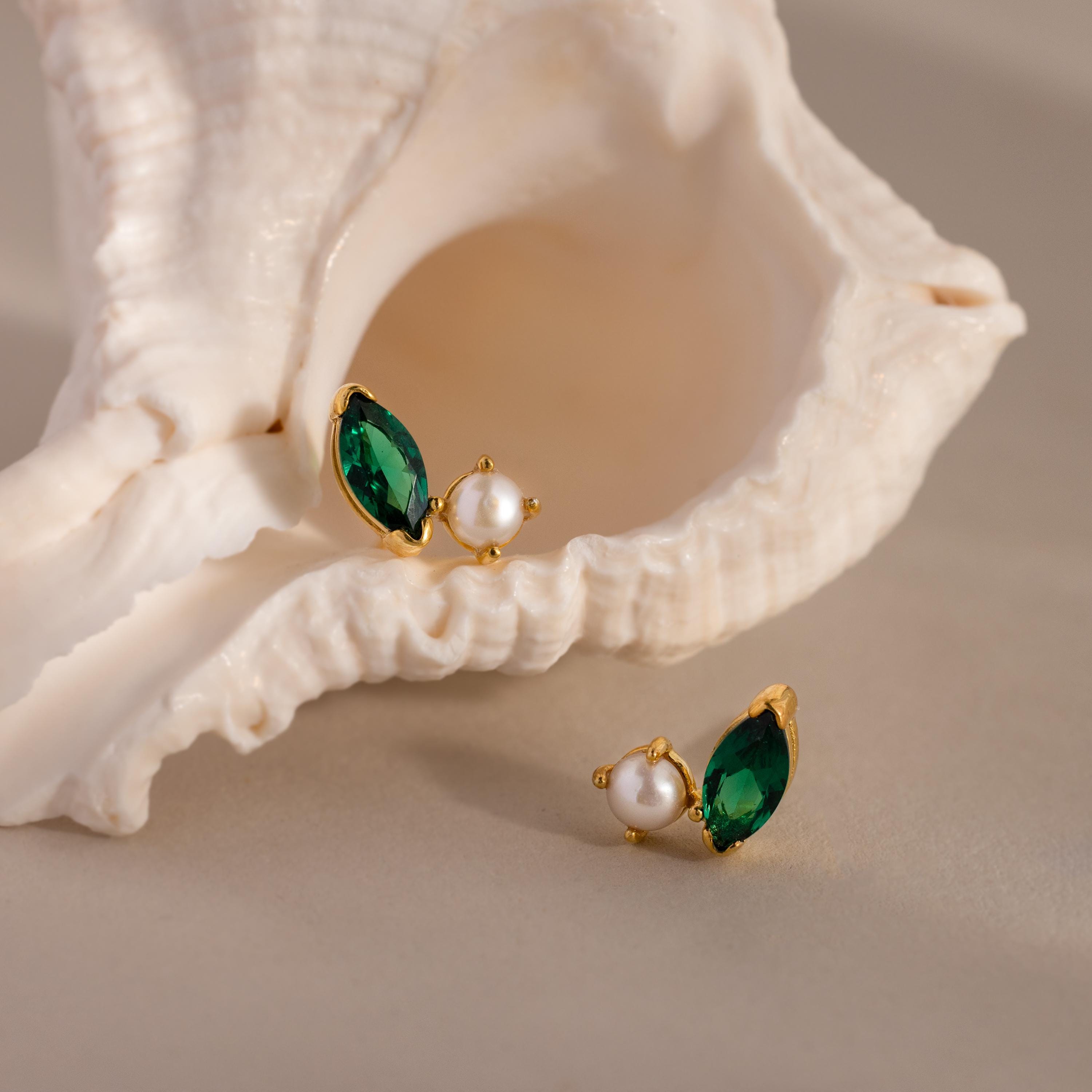 Marquise Birthstone & Pearl Studs—gold earrings featuring green gemstones and pearls, including elegant pearl studs—displayed on and beside a white seashell.
