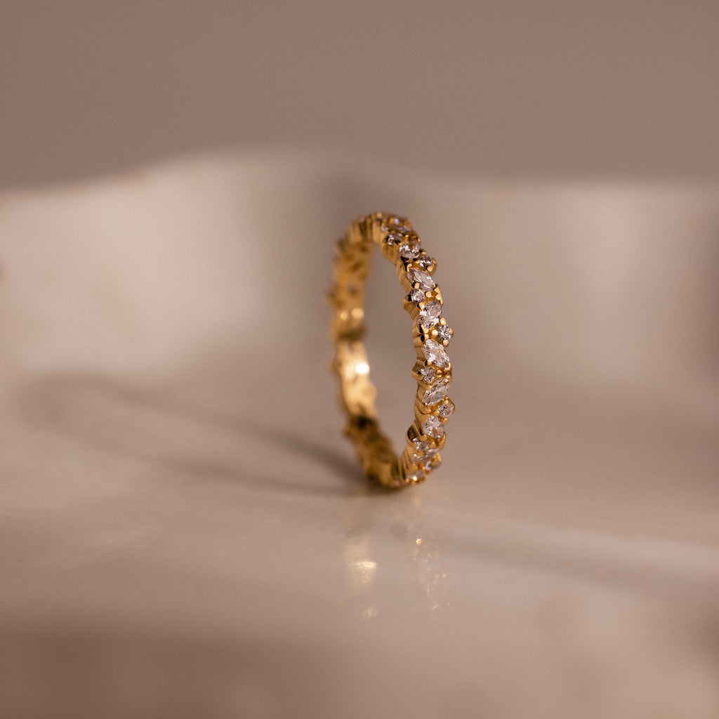 The Diamond Cluster Eternity Ring, featuring small diamonds set all around, is shown on a smooth, light-colored surface.