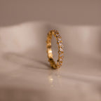 The Diamond Cluster Eternity Ring, featuring small diamonds set all around, is shown on a smooth, light-colored surface.