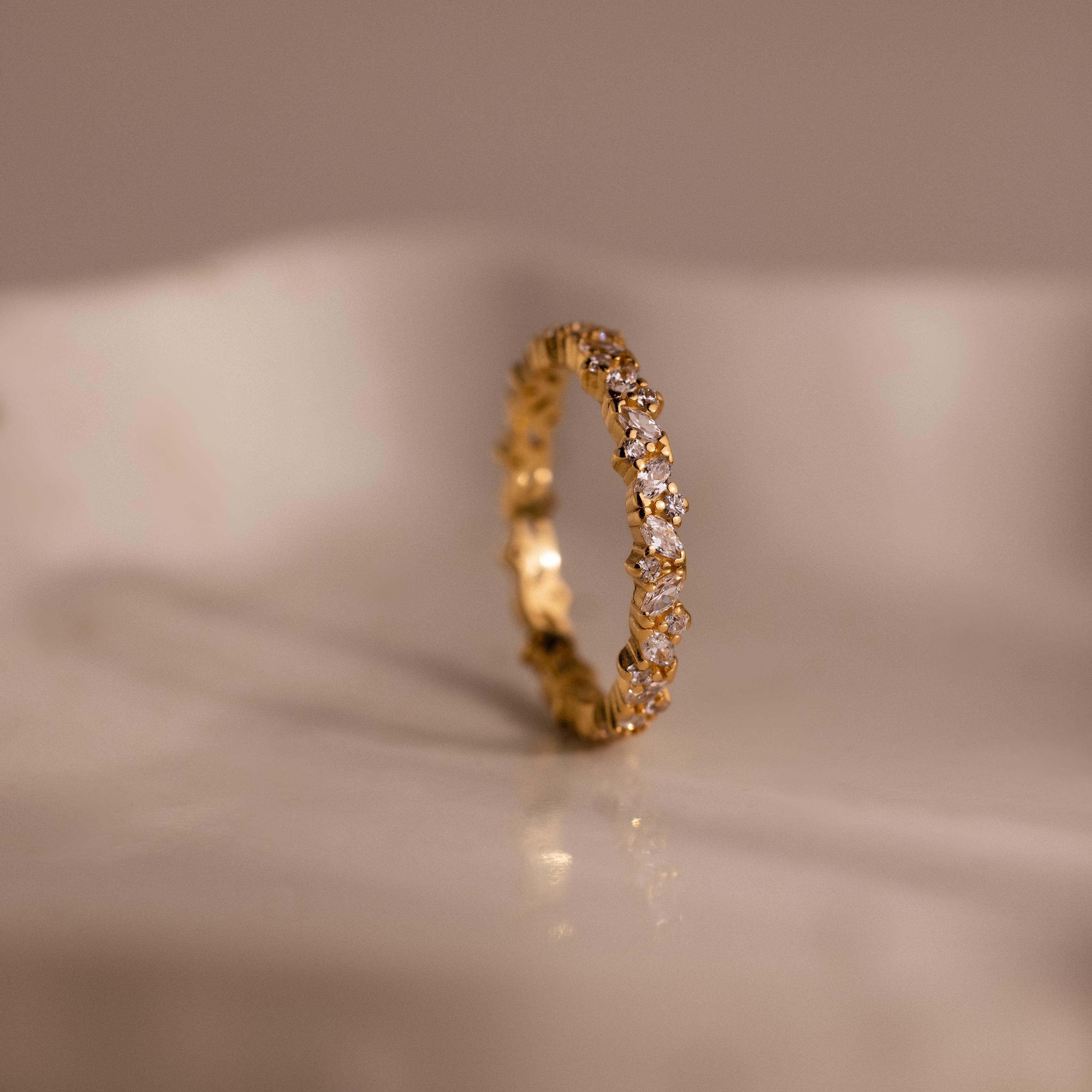 The Diamond Cluster Eternity Ring, featuring small diamonds set all around, is shown on a smooth, light-colored surface.