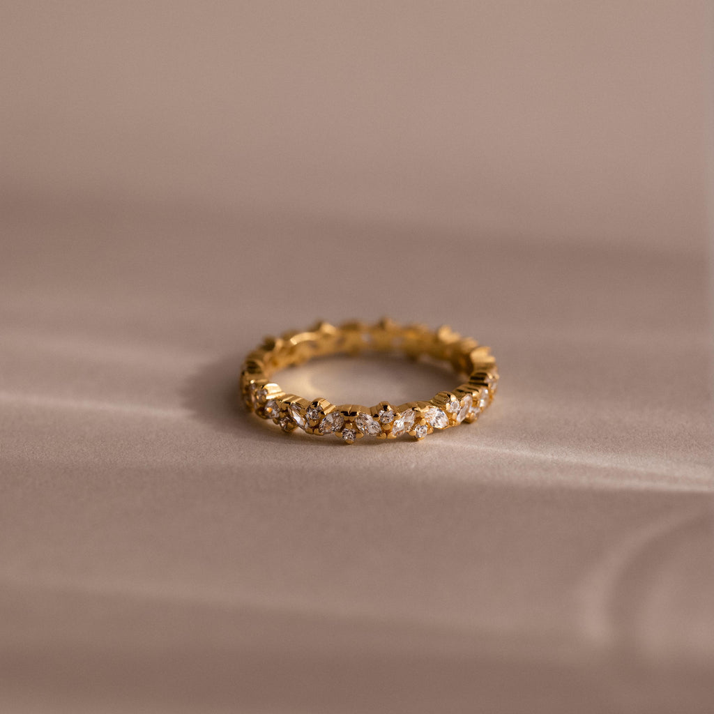 The Diamond Cluster Eternity Ring rests on a soft beige surface, showcasing its brilliant design.