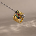 The Multiple Birthstone Band in 18K Gold features four stacked gold rings set with colorful square gemstones, creating a stunning personalized jewelry piece against a neutral background.