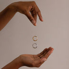 Two hands frame a floating gold ring above a silver ring, highlighting the Mixed Metal Dome Ring Set—a versatile and modern jewelry collection—against a plain beige background.