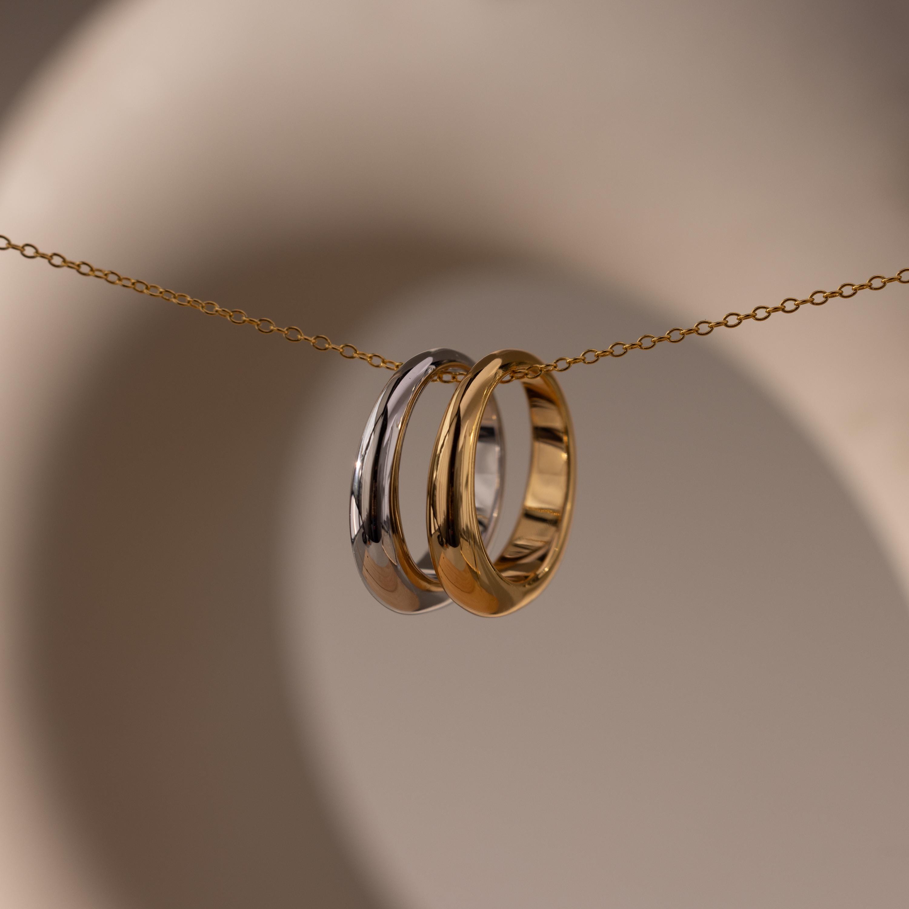 The Mixed Metal Dome Ring Set features a gold and a silver ring together on a delicate gold chain, offering versatile, modern-classic jewelry displayed against a soft beige background.