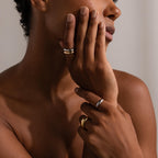 A person with natural nails wears versatile jewelry, including the Mixed Metal Dome Ring Set in silver and gold, gently touching their face.