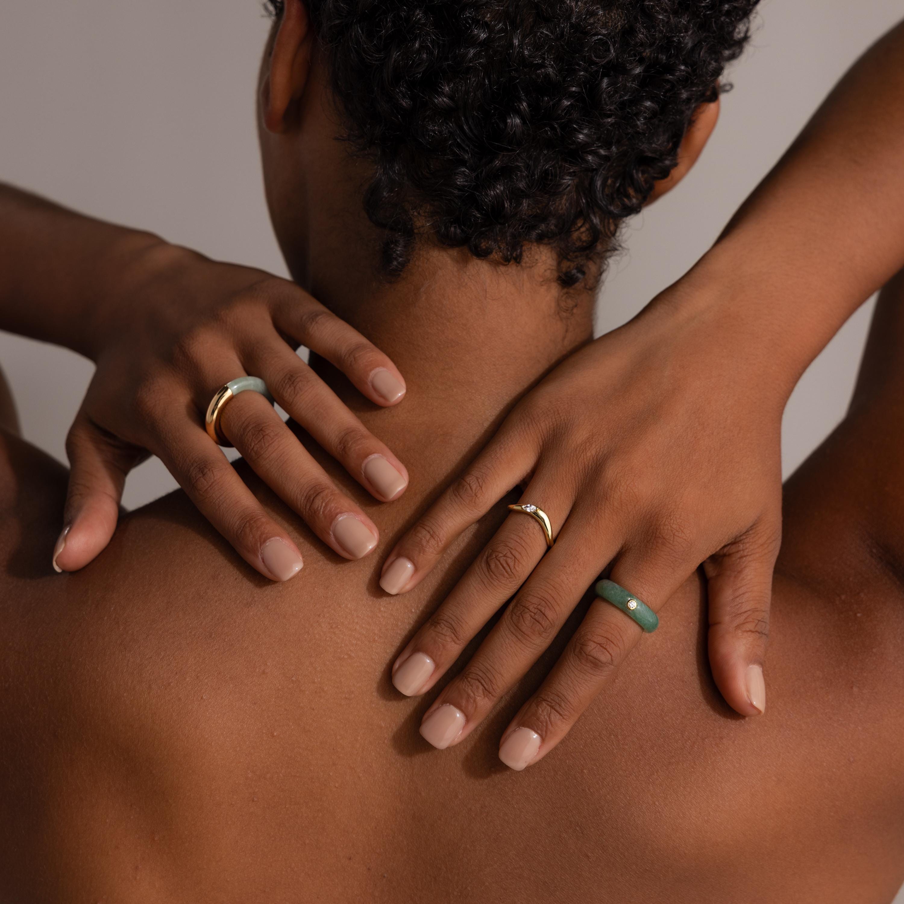 Model with short curly hair, hands on neck, shows her back while wearing the Jade Diamond Ring with a gold bezel and green jade accents.