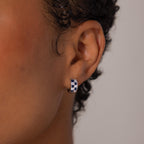 Close-up of a person's ear wearing Royal Blue Checkered Huggies in Sterling Silver, featuring blue and clear stones.