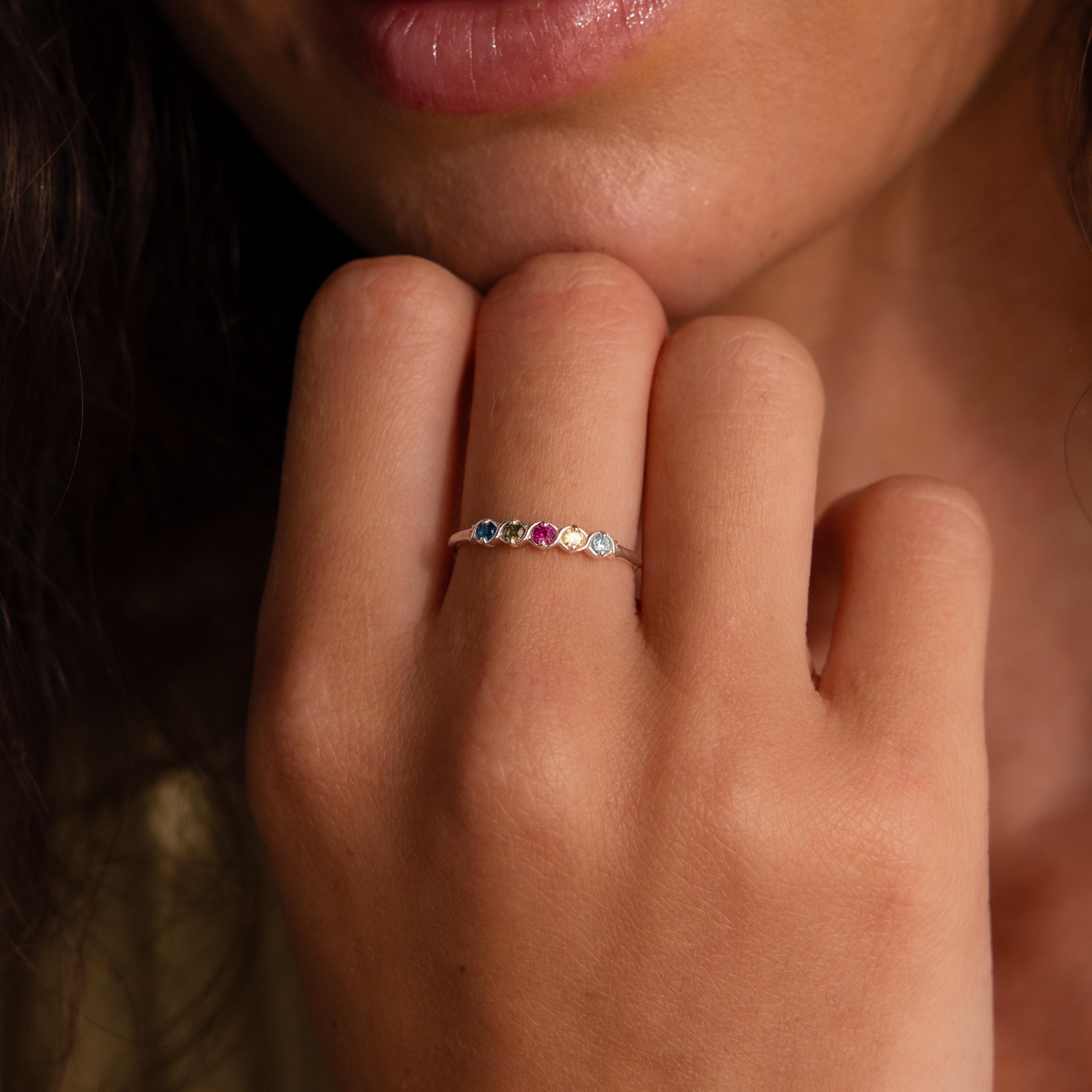 A hand near the lips showcases the Woven Multiple Birthstone Ring in Sterling Silver, a vintage-inspired jewelry piece adorned with colorful gemstones.