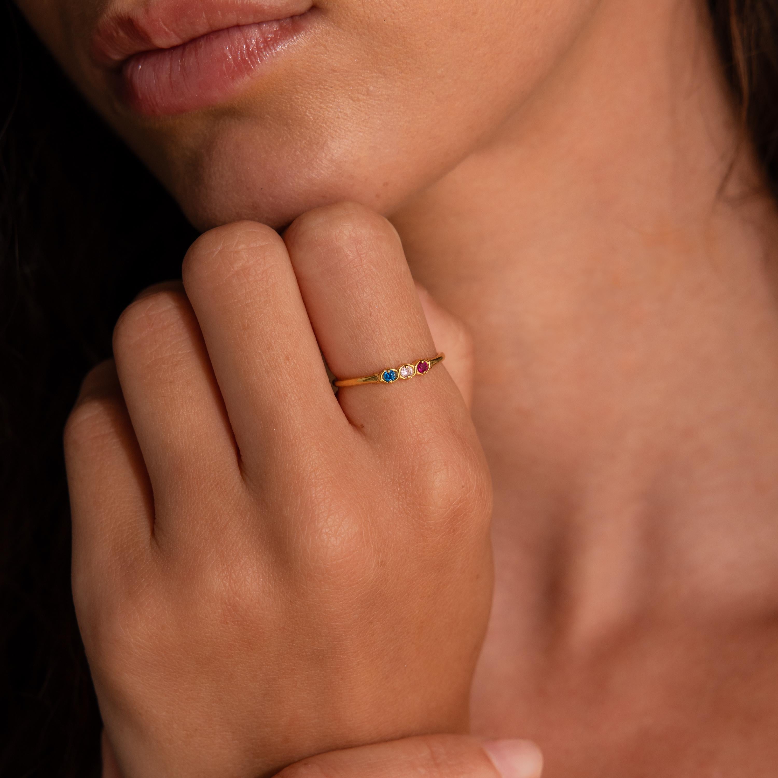 Someone wearing the Woven Multiple Birthstone Ring, a vintage-inspired gold band accented with small colorful gemstones, on their finger near their lips.