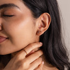Woman with closed eyes wears Birthstone Cluster Flatback Studs and a matching gold ring, gently touching her neck to showcase an elegant earring stack.