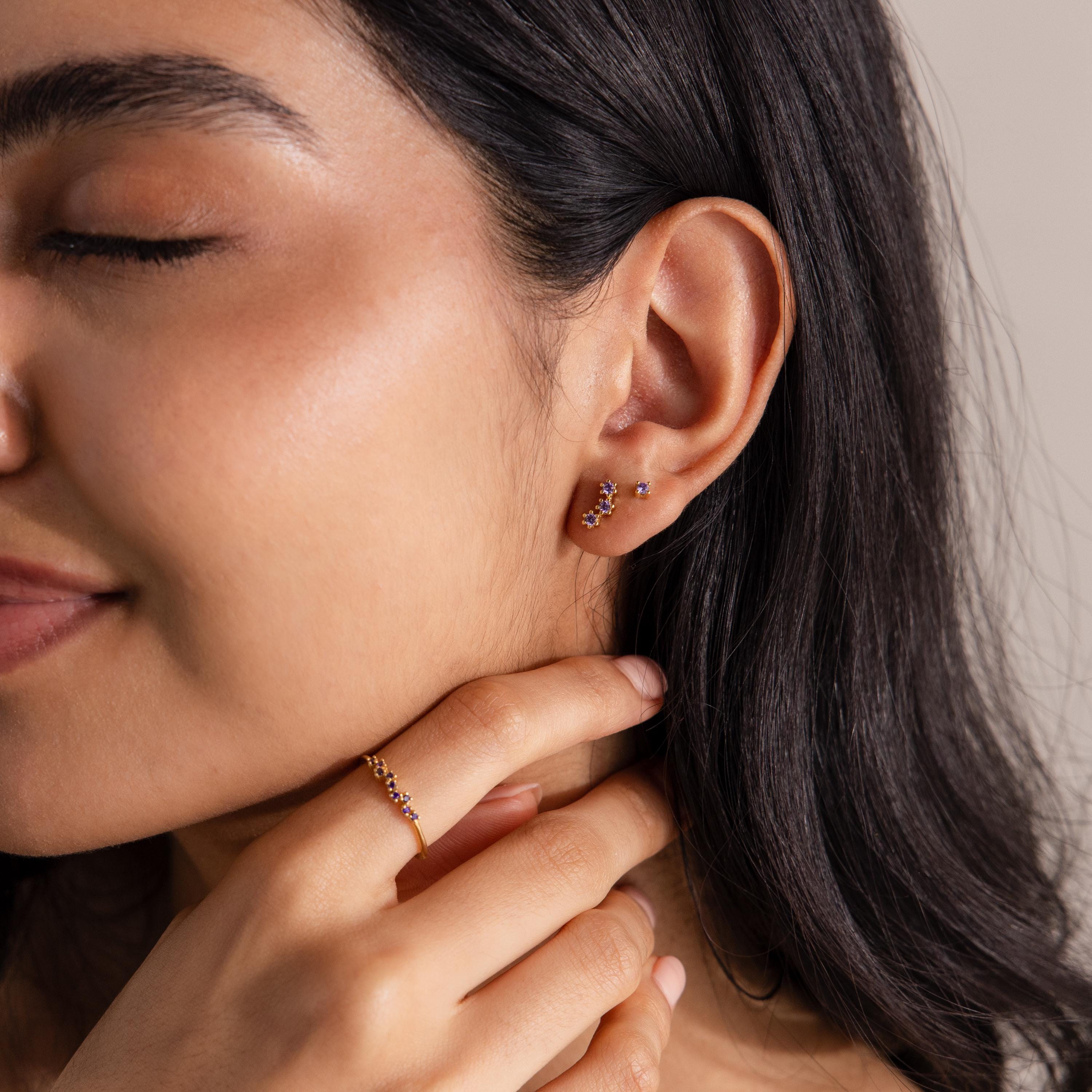 Woman with closed eyes wears Birthstone Cluster Flatback Studs and a matching gold ring, gently touching her neck to showcase an elegant earring stack.