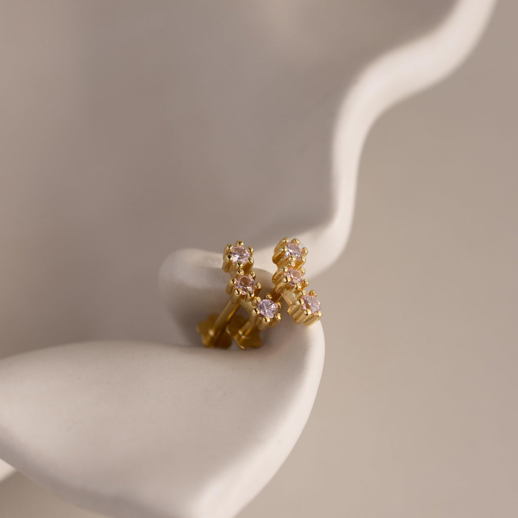 Pink Tourmaline Cluster Flatback Studs featuring small pink and clear gemstones, reminiscent of birthstone earrings, displayed on a smooth, wavy white surface.