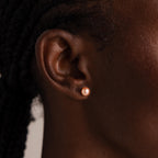 A close-up of an ear adorned with Pink Pearl Studs, delicate freshwater pearl earrings in a soft blush tone, complemented by braided hair.