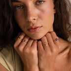 A woman with wavy hair wearing the Multiple Birthstone Band, gently touching her chin and looking at the camera—personalized jewelry to tell your unique story.