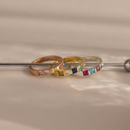 The Multiple Birthstone Band in gold, rose gold, and silver shines on a neutral surface—ideal as personalized jewelry or a unique gift for celebrating multiple birthstones.