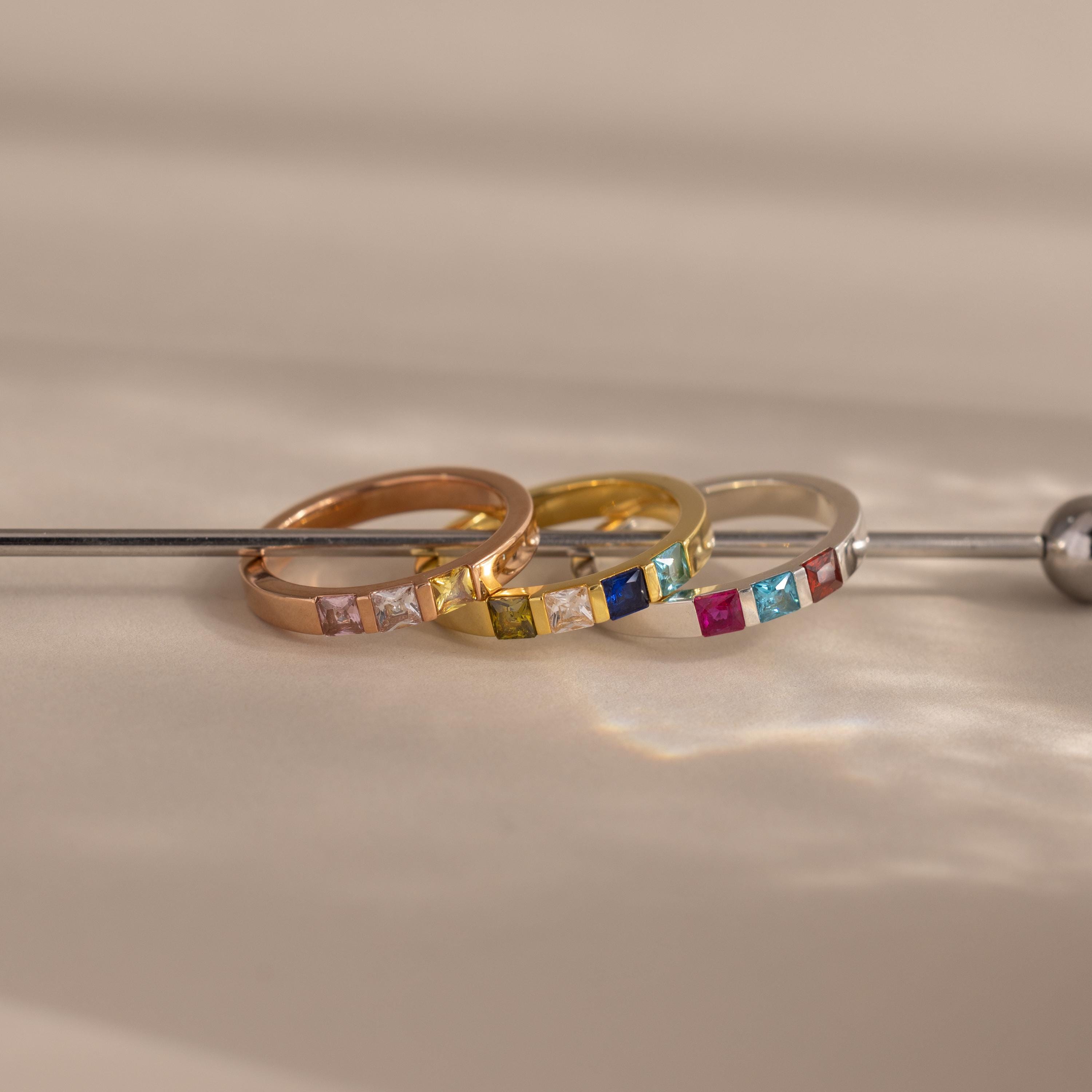 The Multiple Birthstone Band in gold, rose gold, and silver shines on a neutral surface—ideal as personalized jewelry or a unique gift for celebrating multiple birthstones.