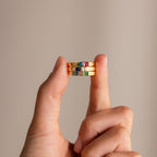 A hand displays three stacked Multiple Birthstone Bands with colorful gemstones, highlighting a personalized jewelry style—ideal as a unique birthstone ring—against a plain background.