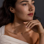 Woman with wavy dark hair gazes thoughtfully to the side, wearing the Jade Bar Jewelry Set in 18K Gold.